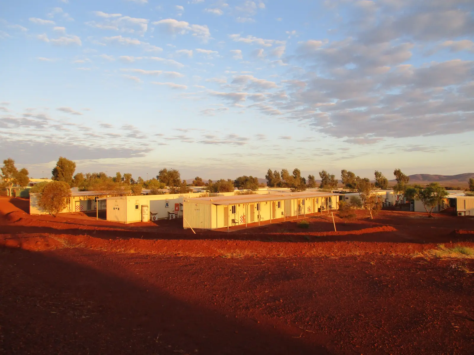 Rows of single-storey accommodation units at a Pilbara mining camp, lit orange by the sunrise