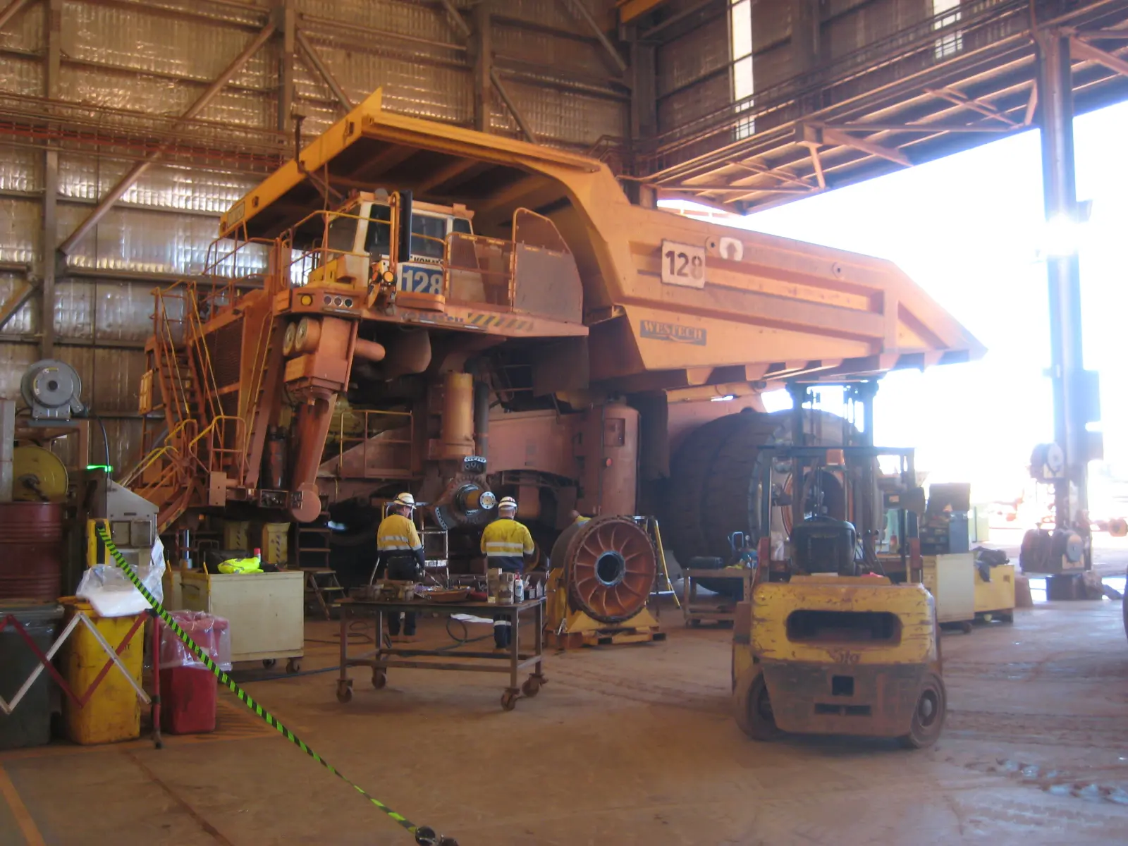 Two maintenance workers in hi-vis and hard hats beside a haul truck stripped down for repair in a mine workshop