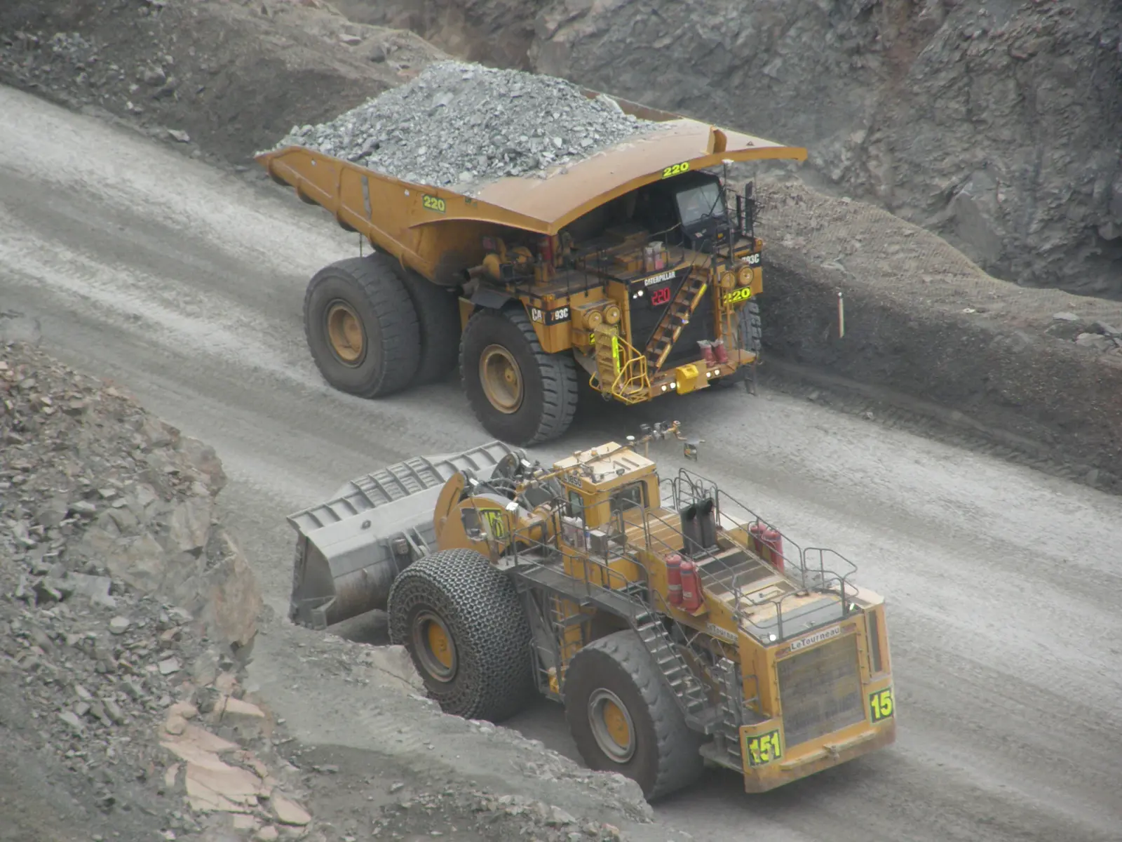 A loaded haul truck passing a large front-end loader on a haul road inside the Super Pit